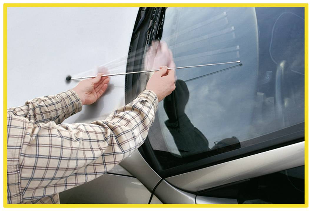 Eine Person reinigt die Windschutzscheibe eines Autos mit einem langen Stabwerkzeug.