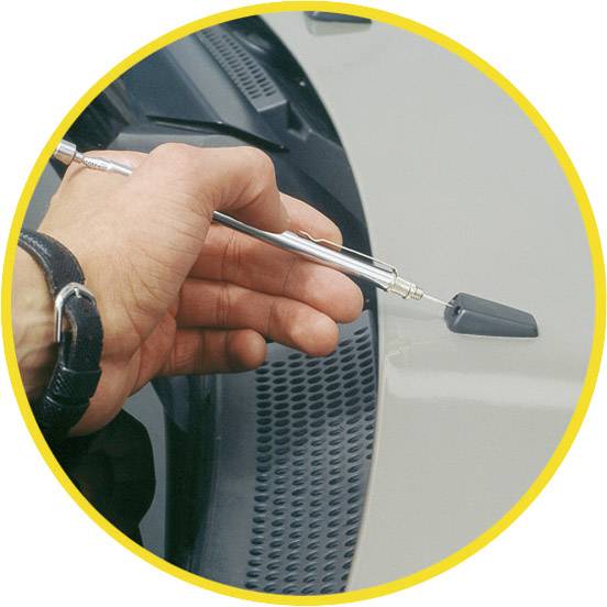 Eine Hand hält ein magnetisches Werkzeug über die Karosserie eines Fahrzeugs, um eine kleine Delle auszurichten.