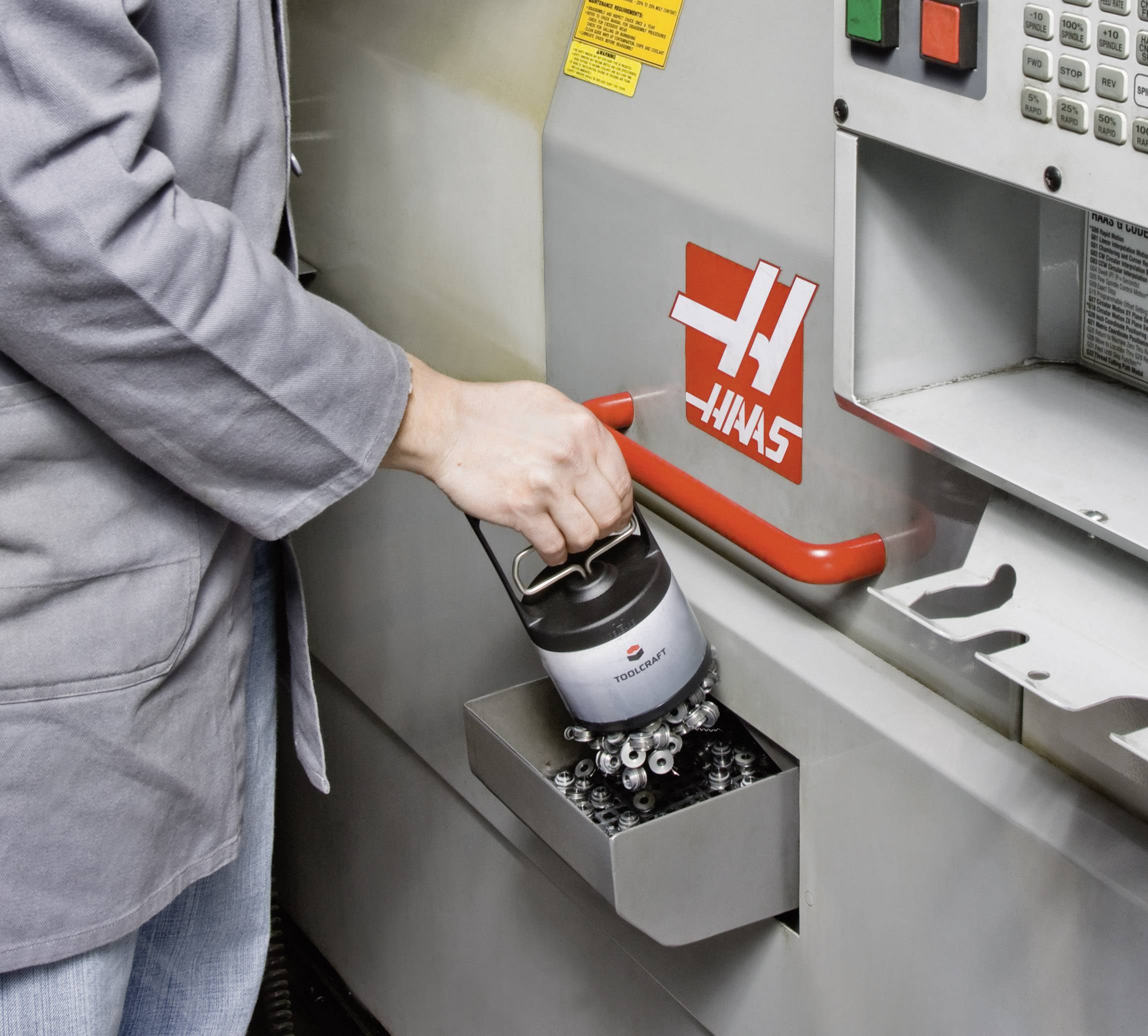 Eine Person entleert einen Behälter mit Metallspänen aus einer CNC-Maschine. Die Maschine zeigt das Logo eines bekannten Herstellers.