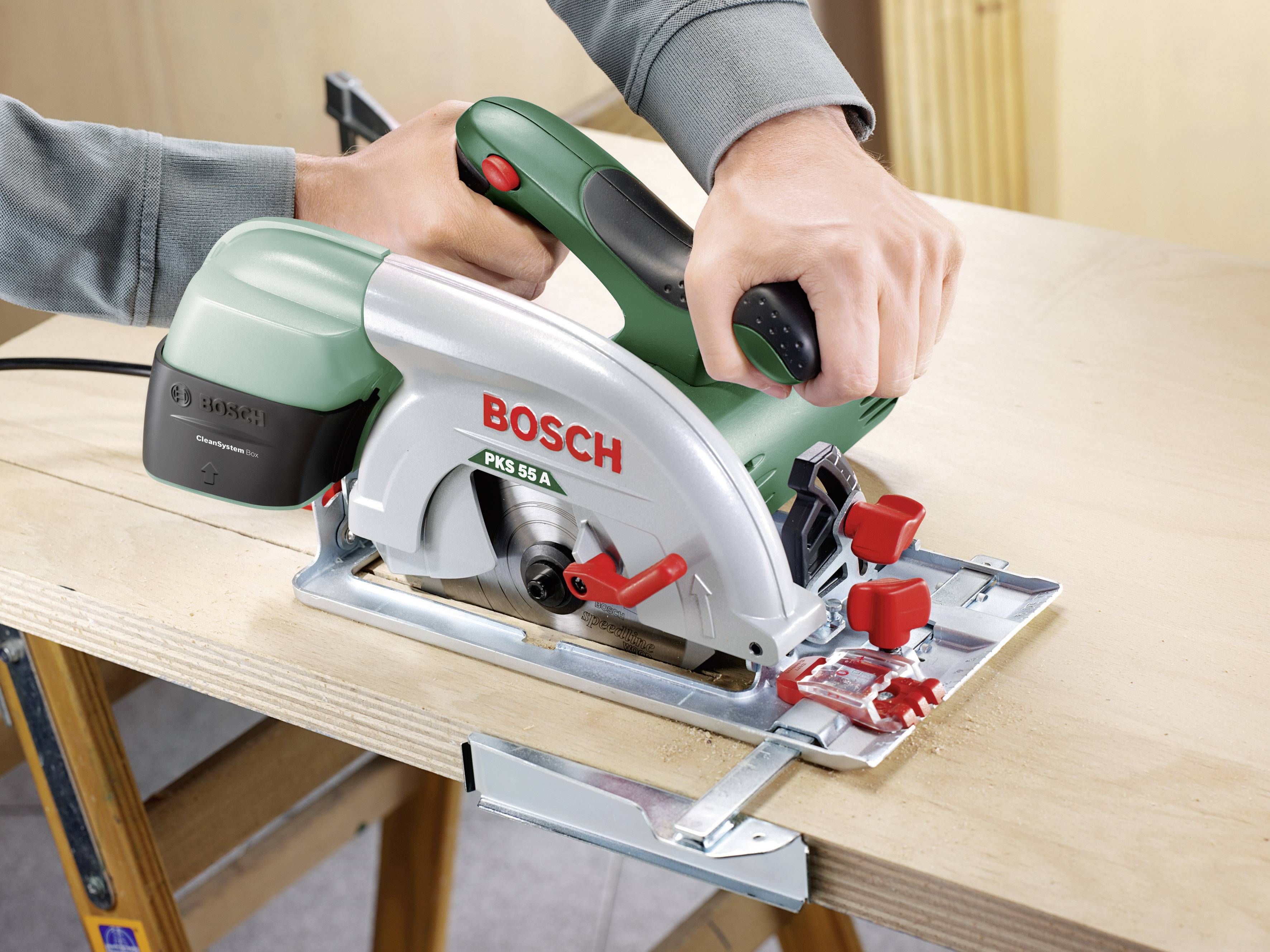 Eine Hand hält eine grüne und silberne Kreissäge der Marke Bosch, die auf einem Holzbrett schneidet.