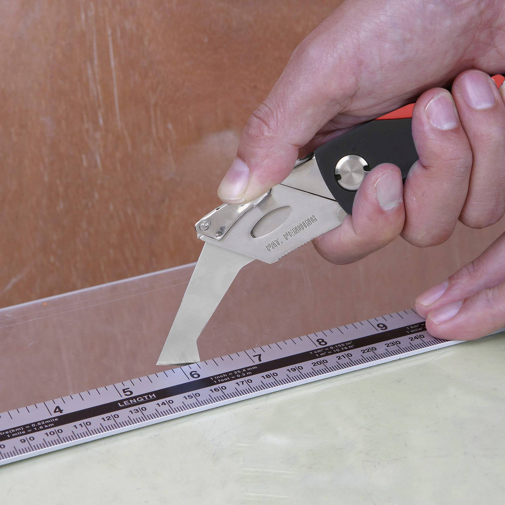 Hand hält ein Cuttermesser und schneidet eine gerade Linie entlang eines Lineals auf einer flachen Oberfläche.