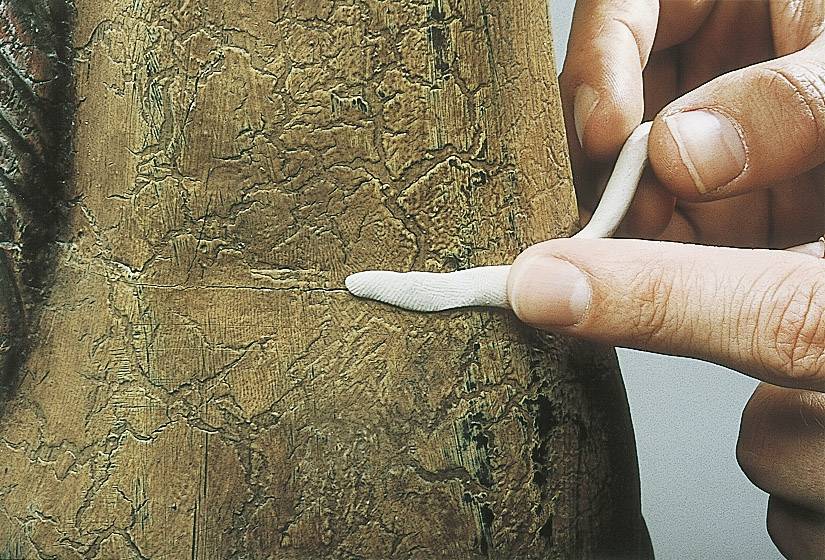 Hände formen eine Masse auf einer brüchigen Oberfläche, möglicherweise bei einer Restaurierung oder Reparatur eines Kunstwerks.