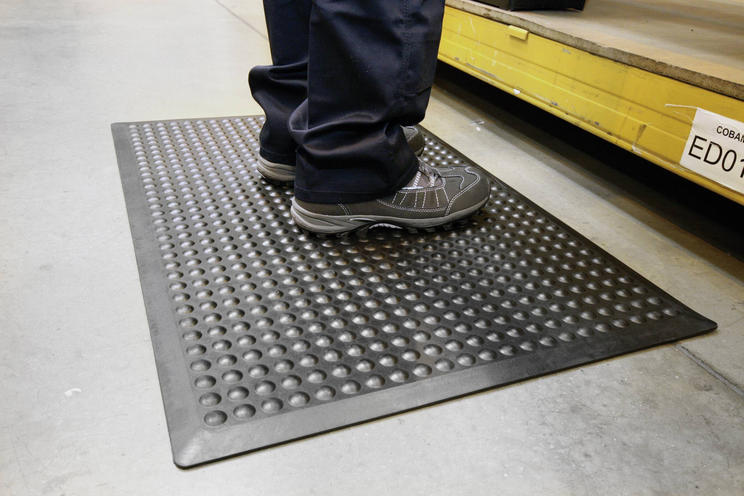 Person steht auf einer rutschfesten Gummimatte in einer industriellen Umgebung, um Ermüdung zu reduzieren und Sicherheit zu gewährleisten.