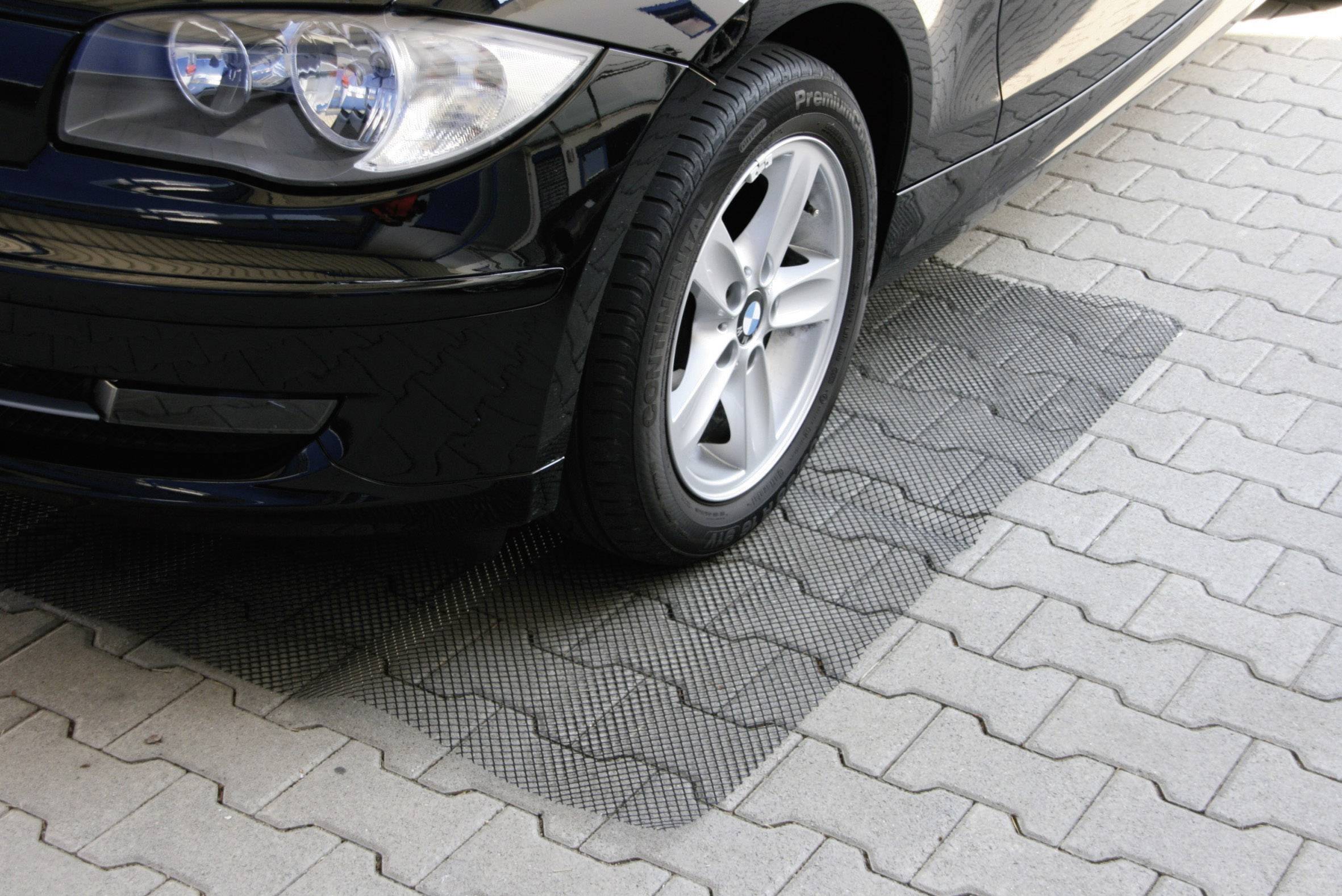 Ein schwarzes Auto parkt auf einem gepflasterten Platz. Der rechte Vorderreifen steht teilweise auf einer strukturierten Gummimatte.