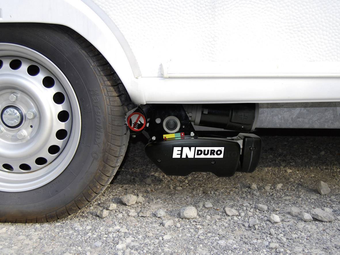 Ein Wohnwagen mit einem montierten Rangierantrieb 'ENDURO' an der Reifenbasis, platziert auf einem kiesigen Untergrund.