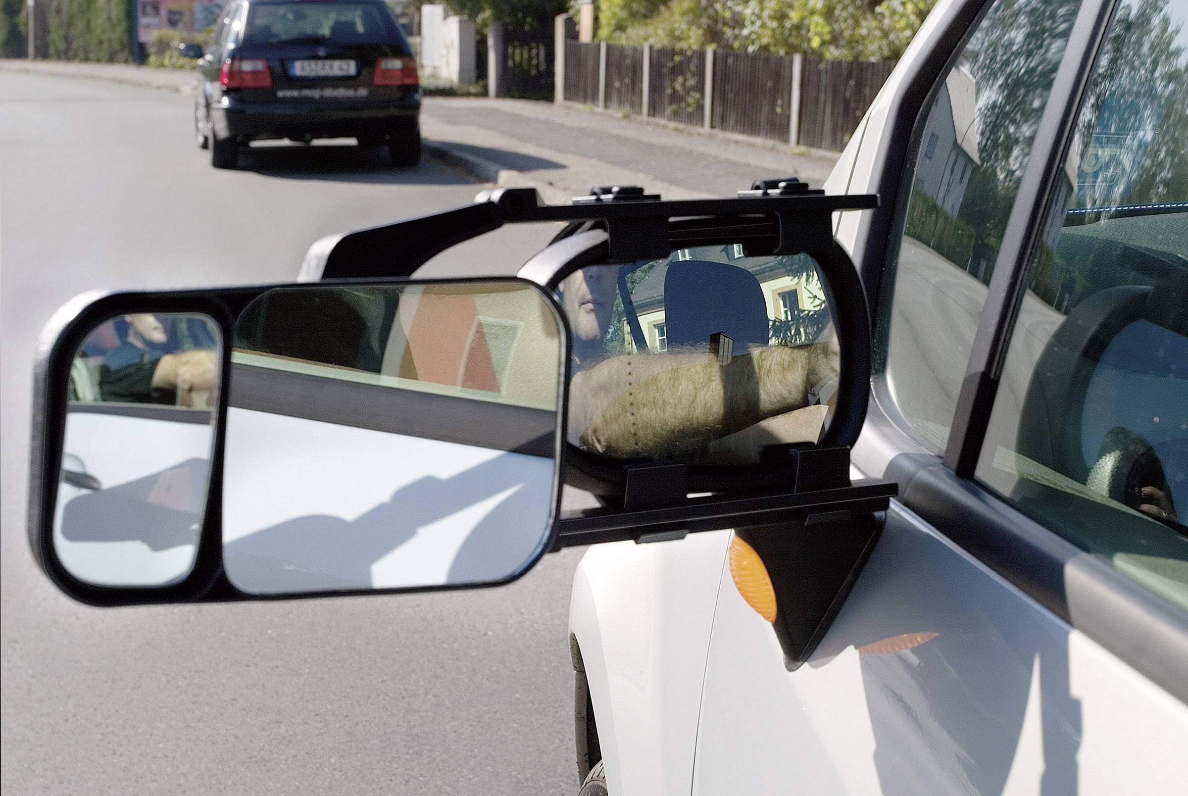 Ein Wohnmobil mit einem zusätzlichen Außenspiegel fährt auf einer Straße. Ein Auto folgt ihm hinterher.