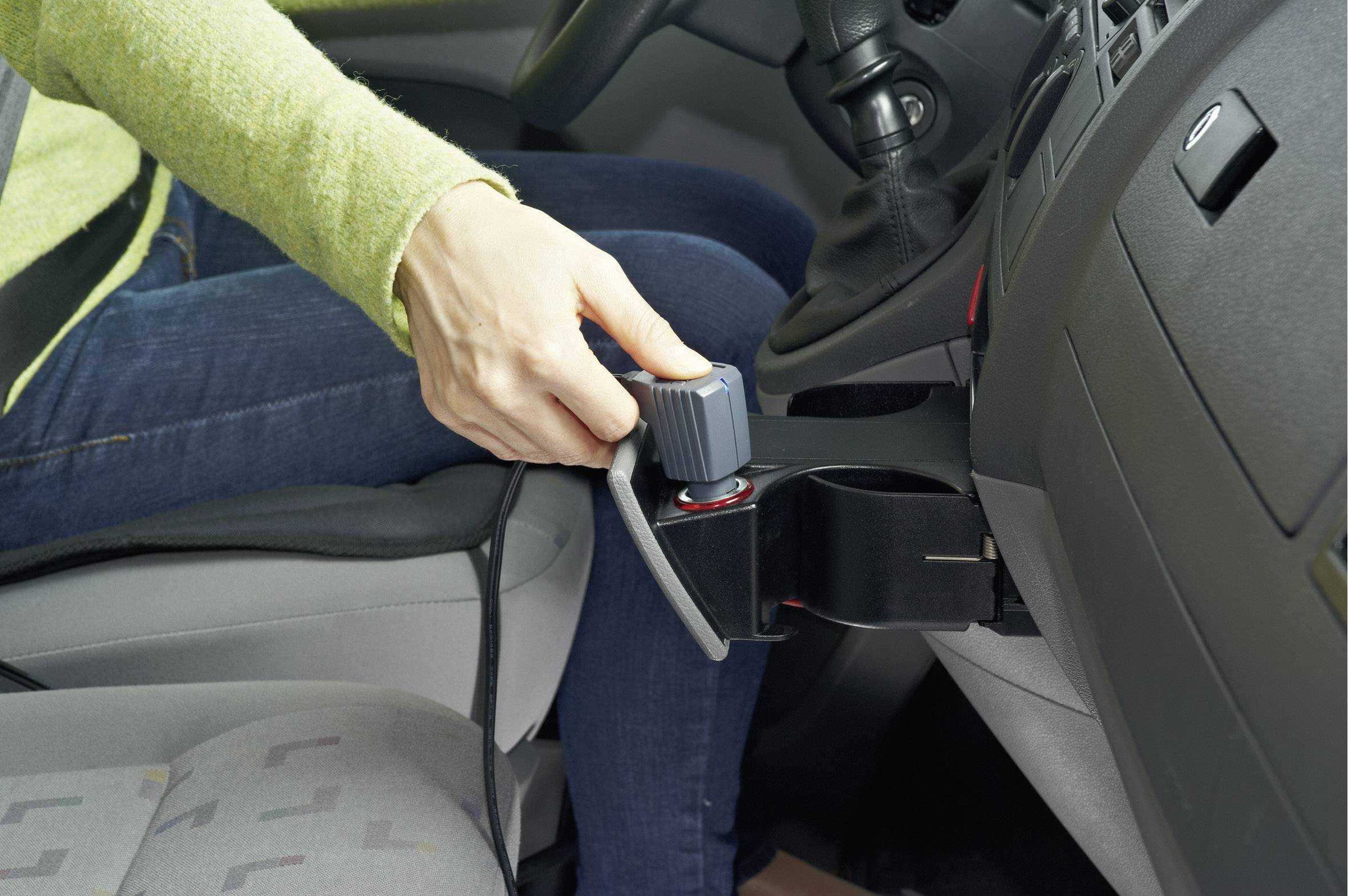 Eine Person im Auto hält ein Handgerät, das an der Mittelkonsole befestigt ist. Es scheint sich um eine manuelle Steuerung zu handeln.
