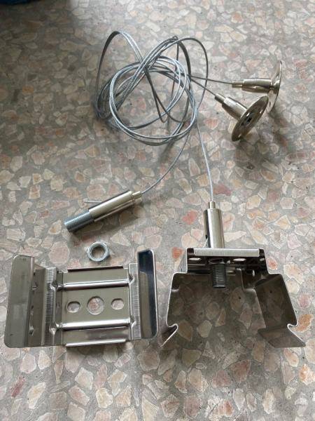 Metallteile und Drähte liegen auf einer gemusterten Oberfläche. Zu sehen sind Klammern, ein Kabel mit zwei Anschlüssen und ein Schraubenadapter.