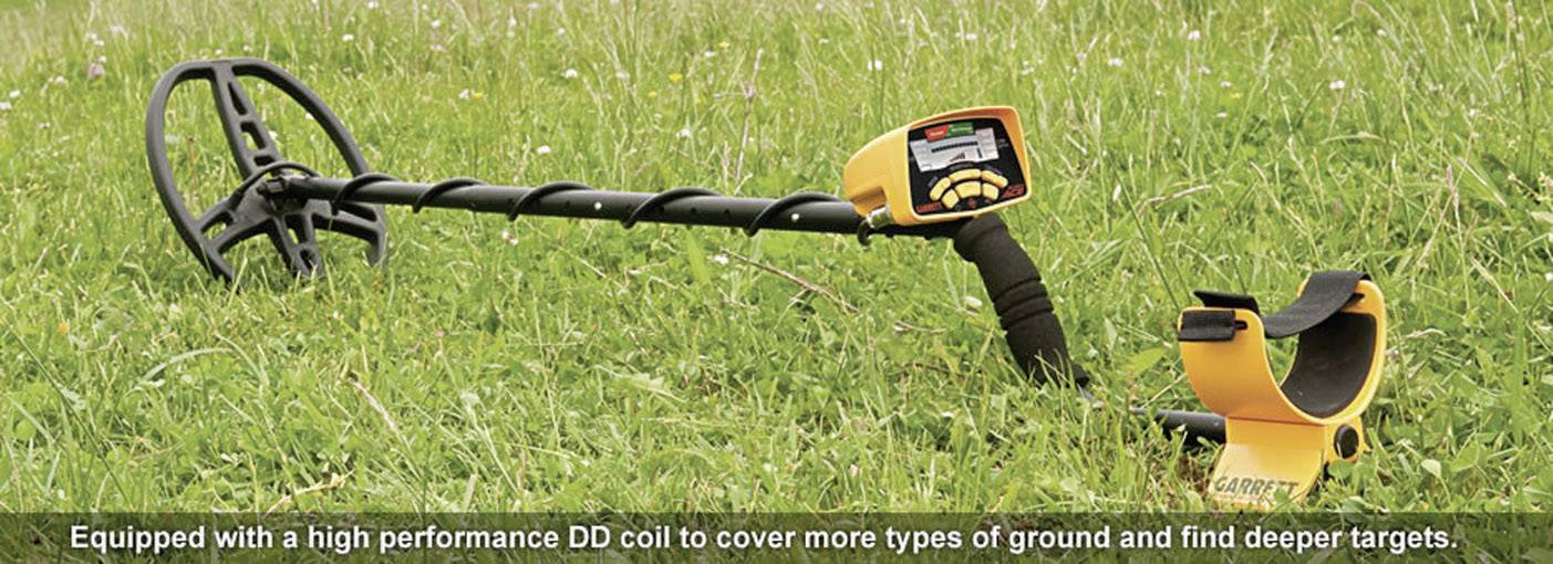 Metallsuchgerät liegt auf einer Wiese. Im Vordergrund ist ein kleinerer orangefarbener Gegenstand platziert. Text: 'Equipped with a high performance DD coil to cover more types of ground and find deeper targets.'
