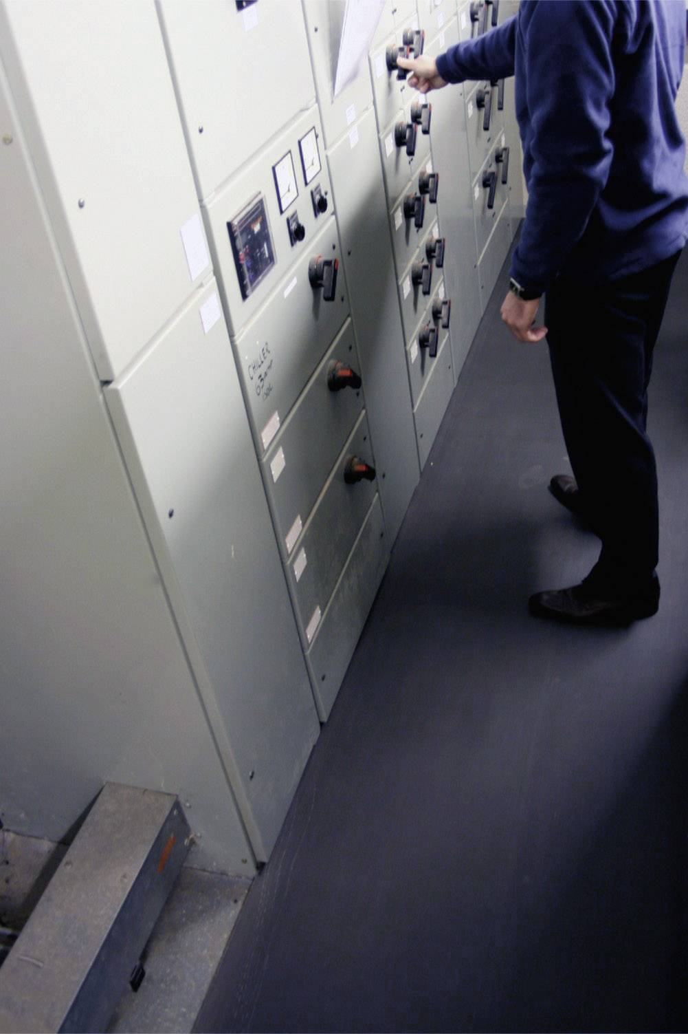 Eine Person betätigt Schalter an einem Schaltschrank in einem technischen Raum. Die Wände sind mit Bedienungselementen ausgestattet.