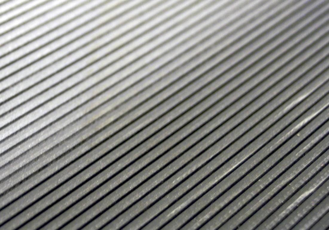 Nahaufnahme einer gerillten, grauen Oberfläche. Die parallelen Linien verlaufen diagonal über das Bild und erzeugen ein schlichtes, strukturiertes Muster.