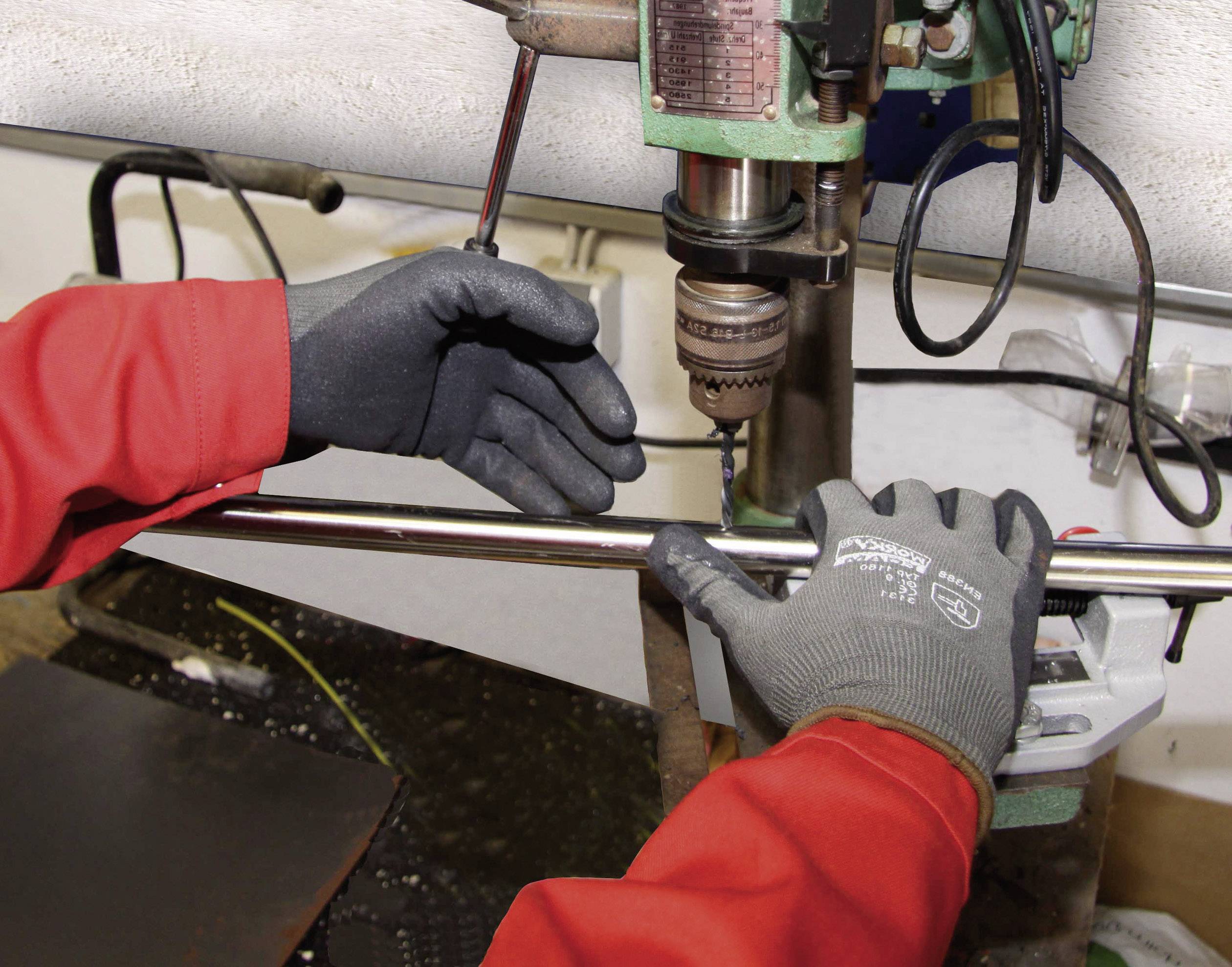 Person mit roten Arbeitshandschuhen bedient eine Ständerbohrmaschine in einer Werkstatt. Fokus auf Sicherheit und Präzision.