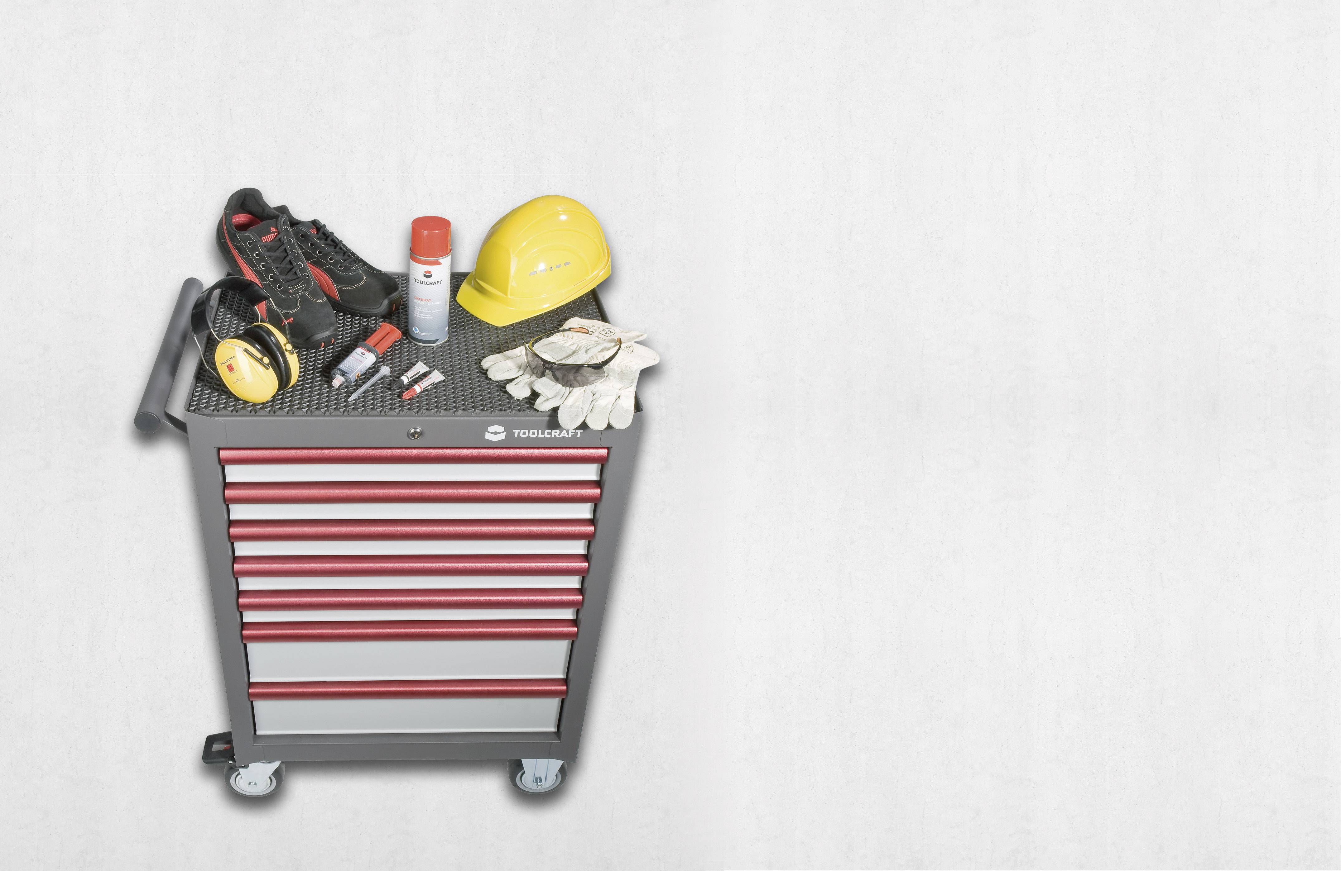 Werkzeugwagen mit roten Schubladen, darauf Schutzhelm, Arbeitsschuhe, Handschuhe und Spraydose, auf grauem Hintergrund.
