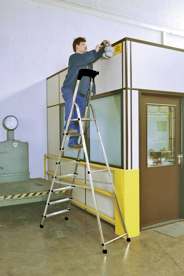 Eine Person steht auf einer hohen Aluminiumleiter und montiert oder repariert etwas oben an einer Trennwand in einem Industriebereich.