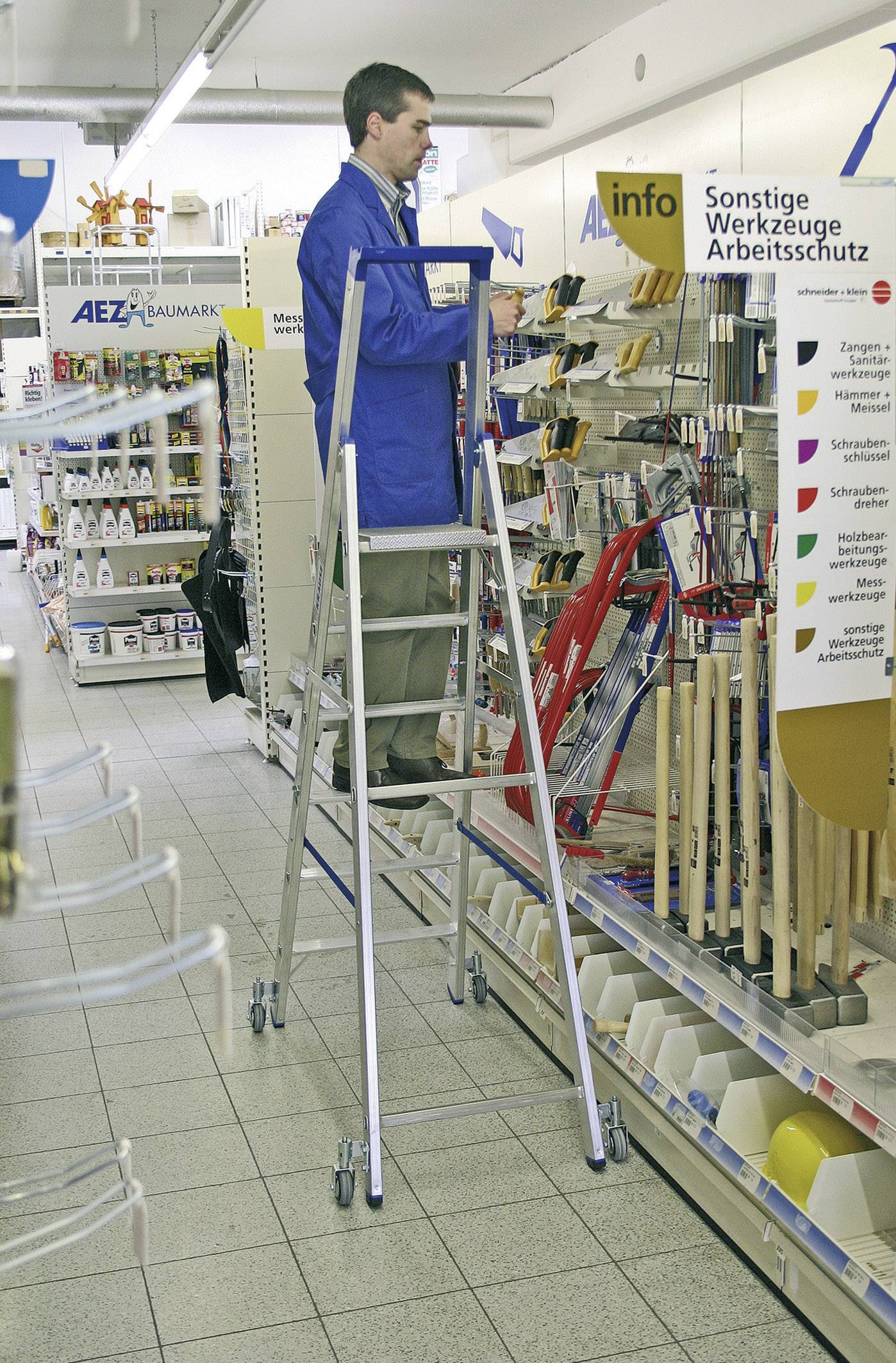 Eine Person steht auf einer Leiter in einem Baumarkt und ordnet Werkzeuge ein. Links im Hintergrund sind Regale mit diversen Artikeln.