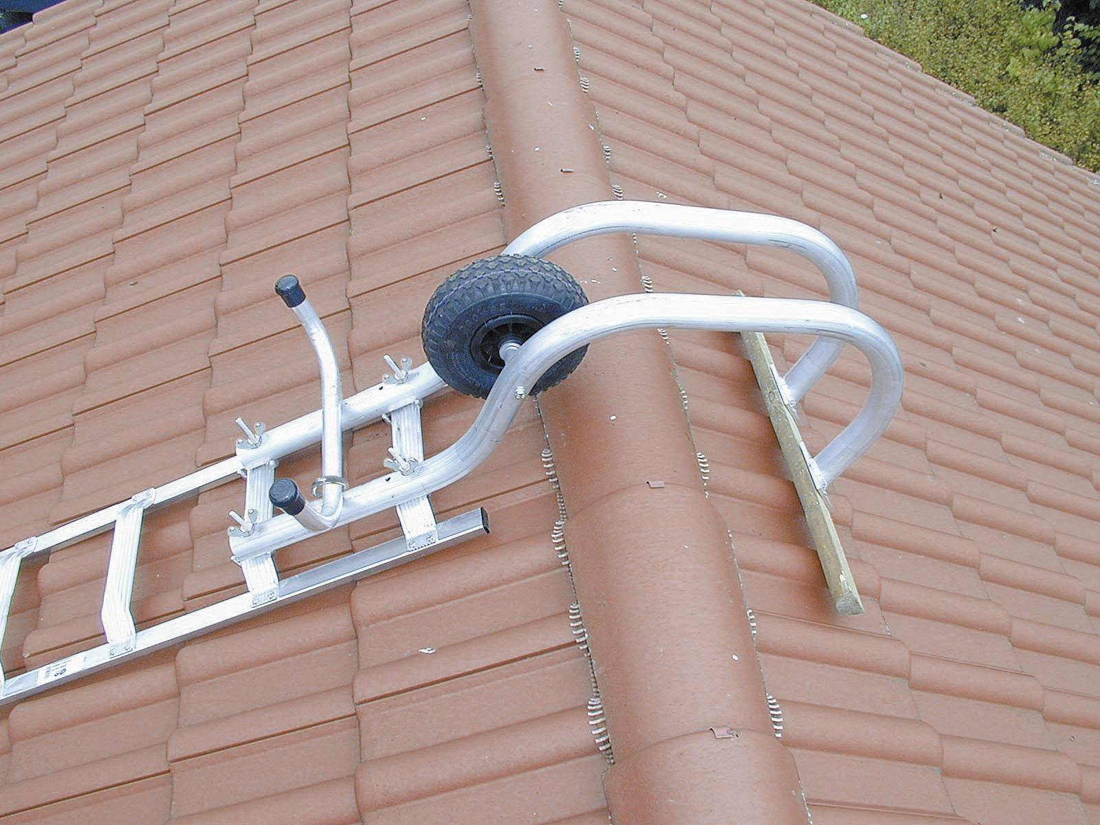 Eine Metallleiter mit einem Rad liegt quer auf einem Ziegeldach. Die Leiter scheint zum Erreichen höherer Stellen auf dem Dach verwendet zu werden.