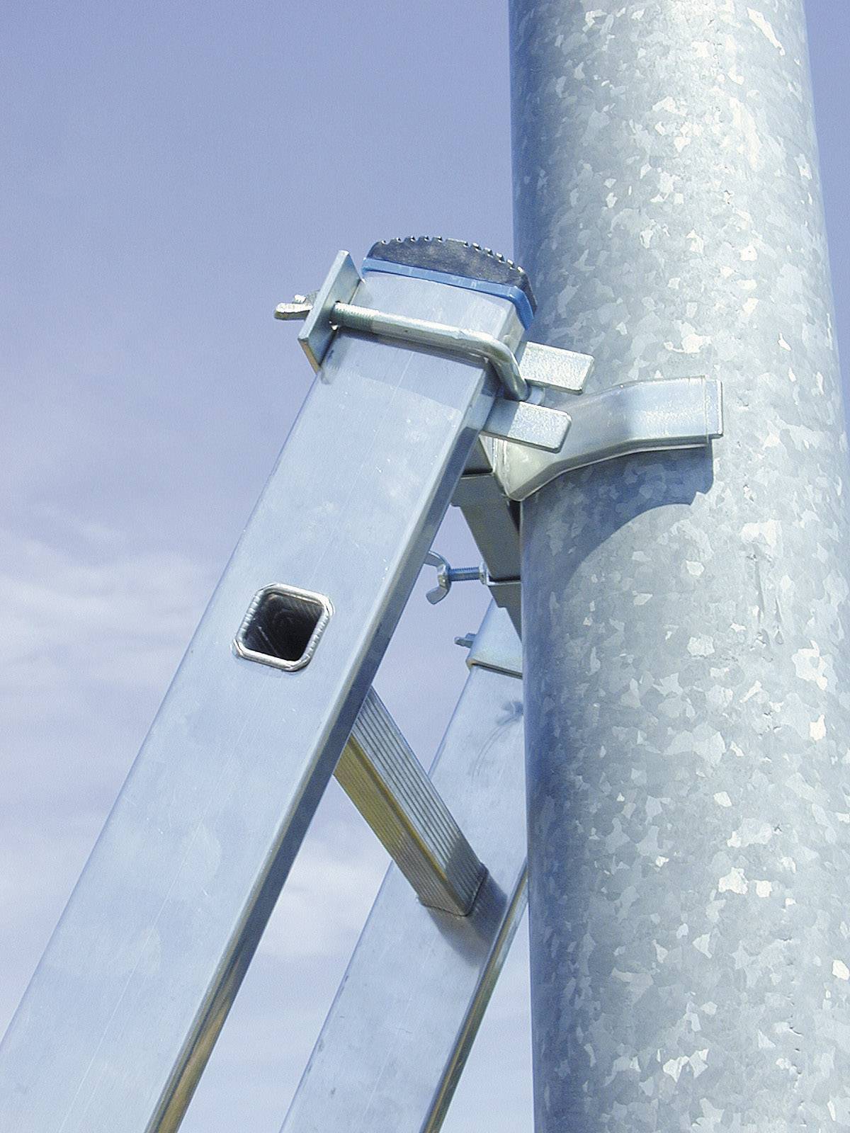 Nahaufnahme eines verzinkten Metallgestänges, das an einem großen Metallrohr befestigt ist, vor blauem Himmel.