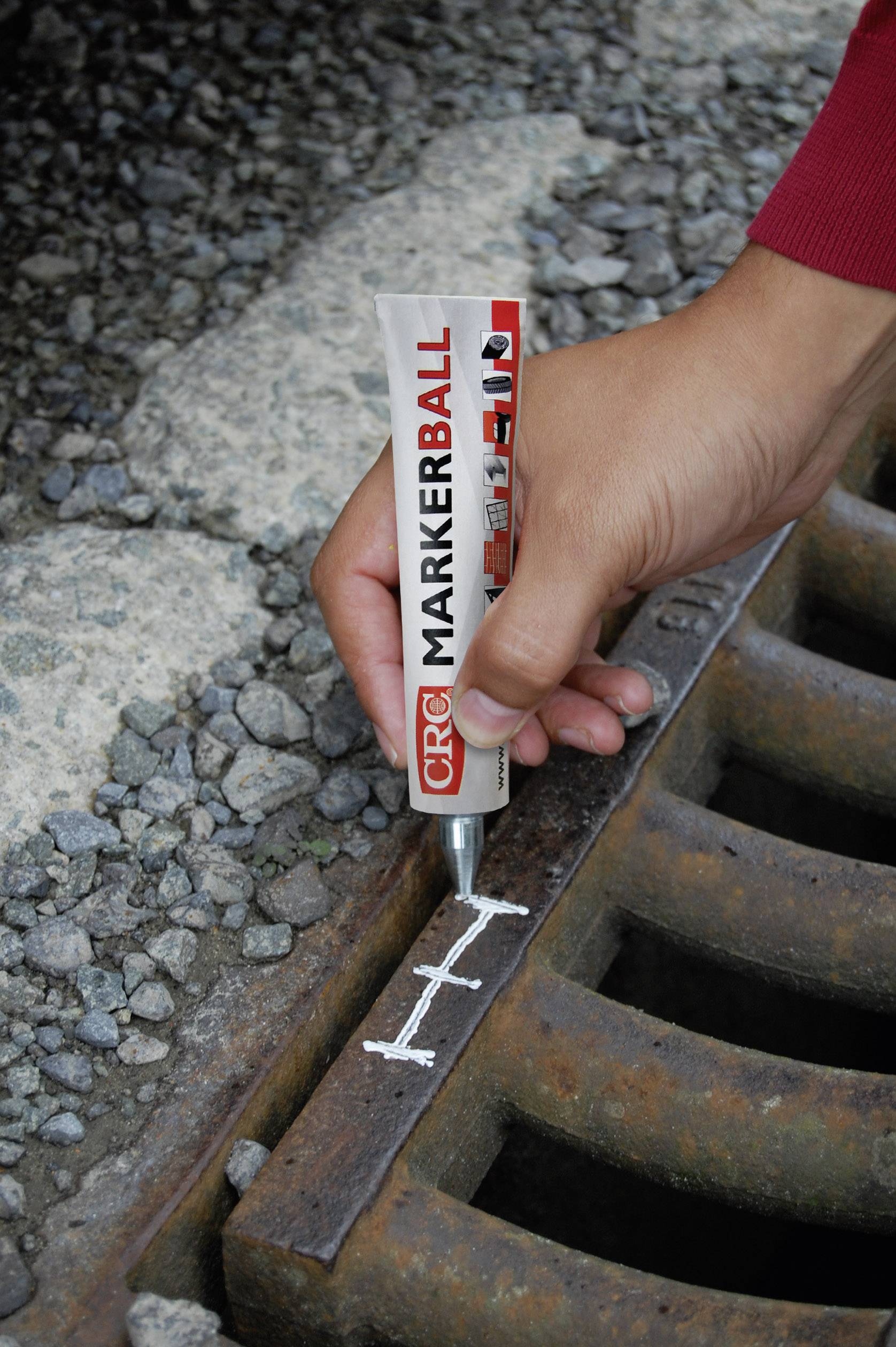 Hand zeichnet weiße Linie auf Metallgitter mit Marker, um Rost anzuzeigen. Schotter im Hintergrund.