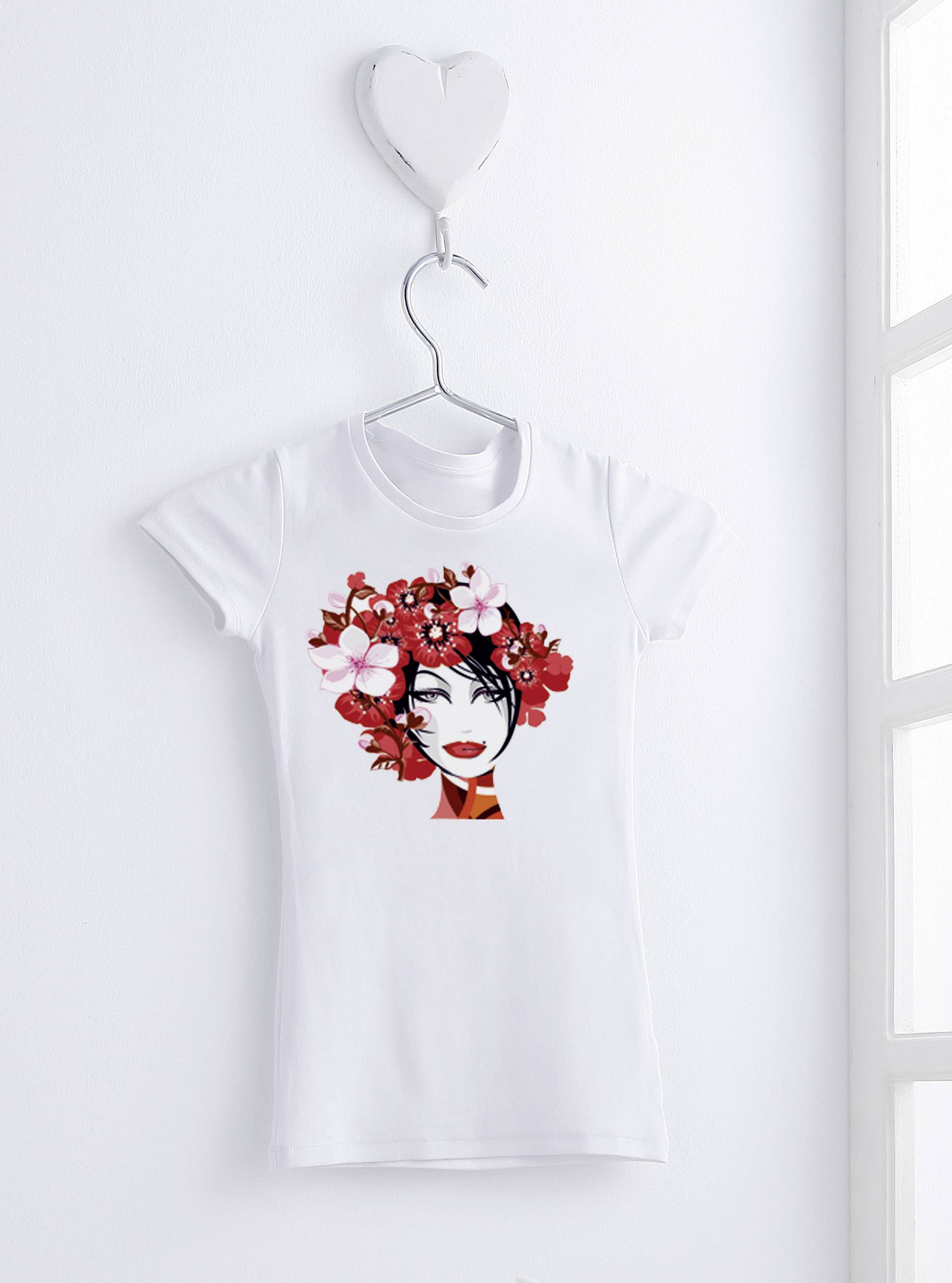 Ein weißes T-Shirt mit einem stilisierten Porträt einer Frau, geschmückt mit roten Blumen, hängt an einem herzförmigen Haken an der Wand.