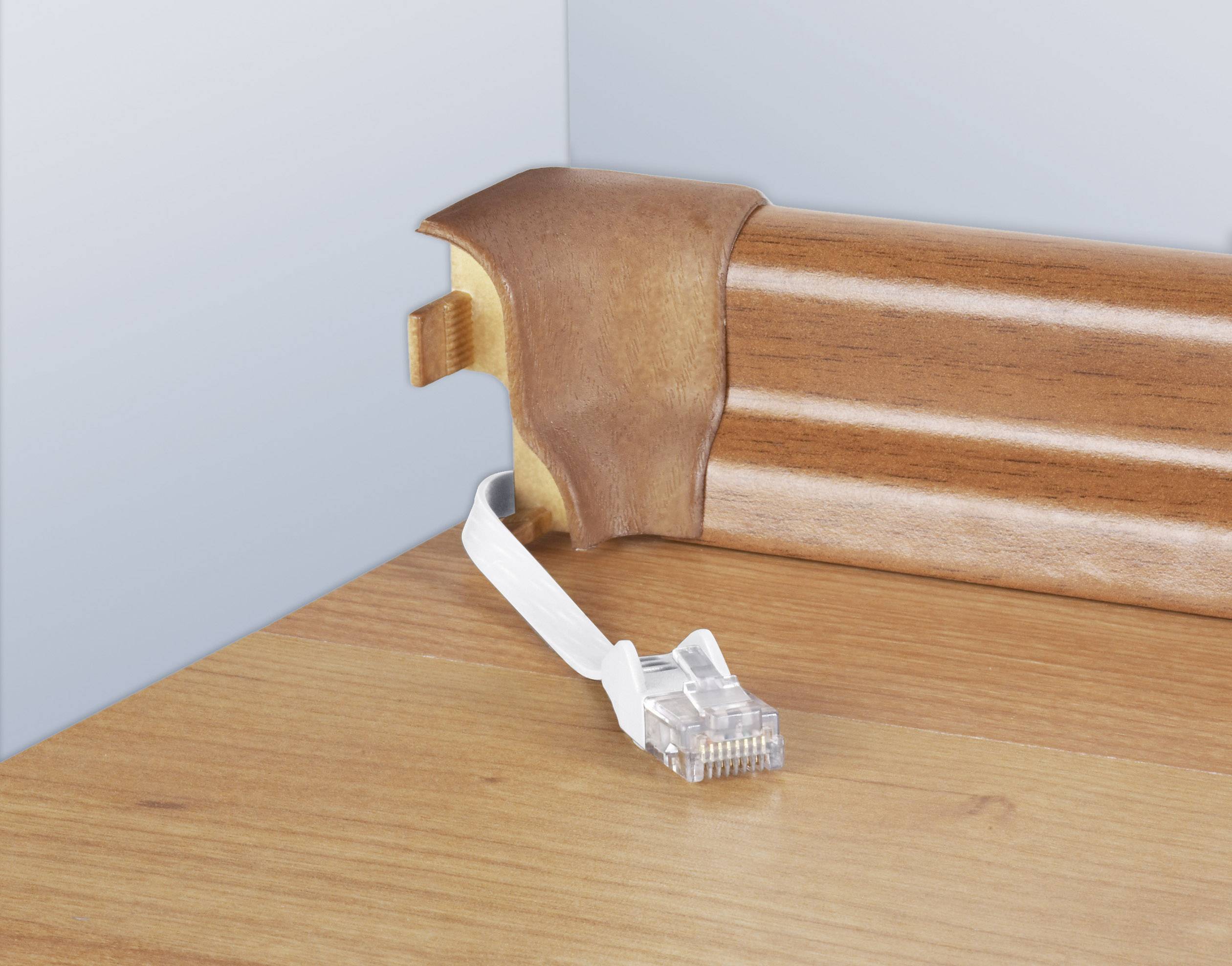 Ein Netzwerkkabel endet an einer Holzfußleiste mit einer kleinen Aussparung, durch die das Kabel führt, passend zur Holzoptik des Bodens.