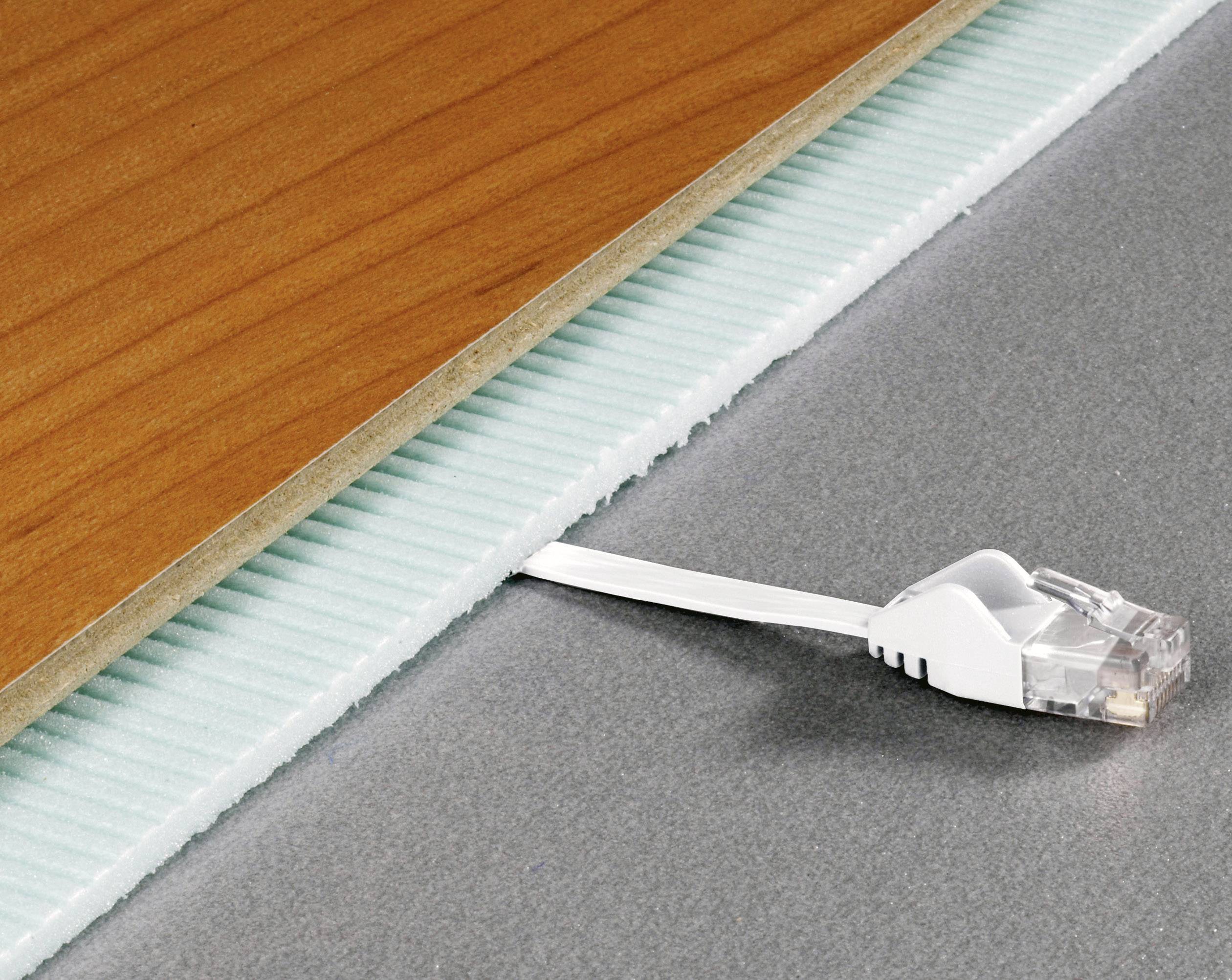 Ein flaches Netzwerkkabel unter einer Holzplatte und einer blauen Dämmplatte auf grauem Untergrund.