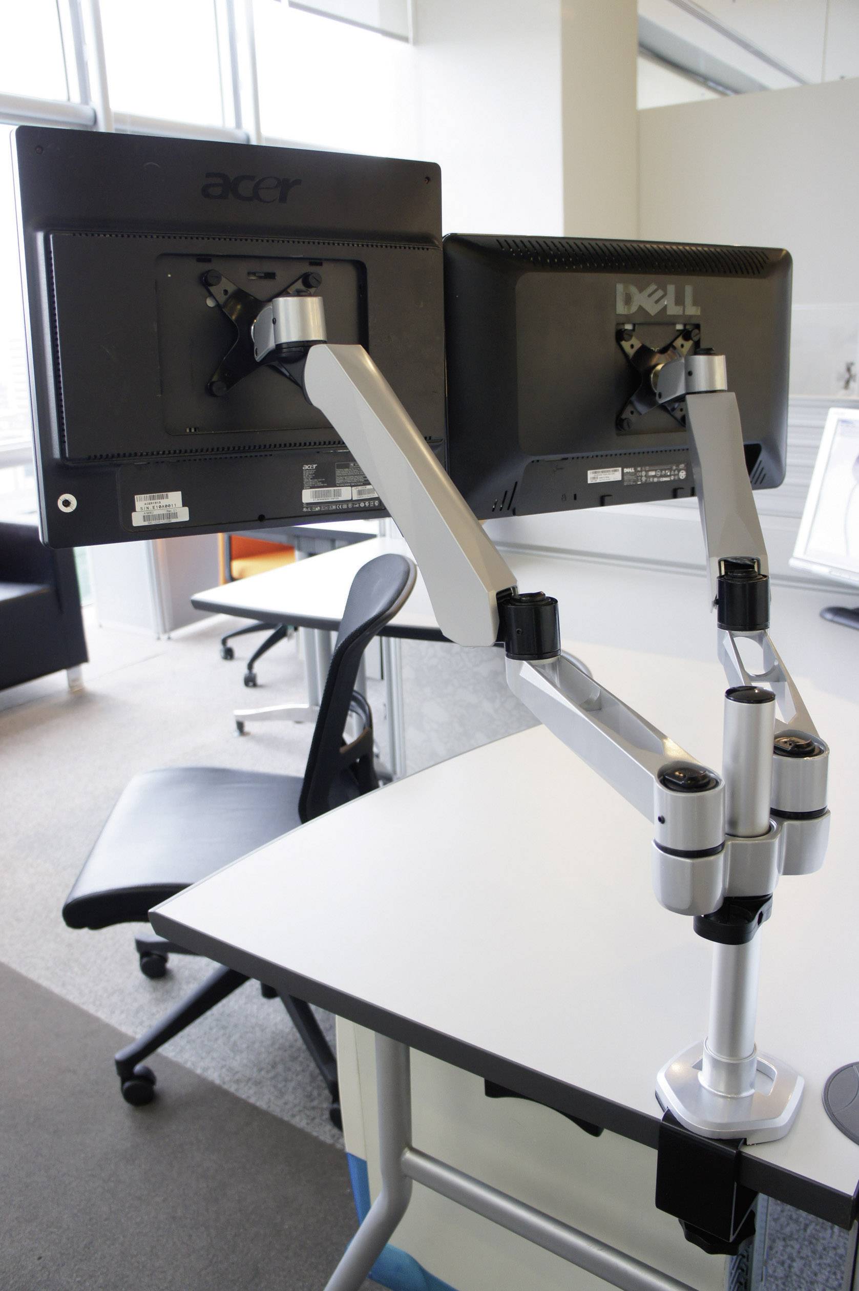 Ein moderner Arbeitsplatz mit zwei Monitoren auf eleganten, verstellbaren Halterungen an einem weißen Schreibtisch in einem Büro.