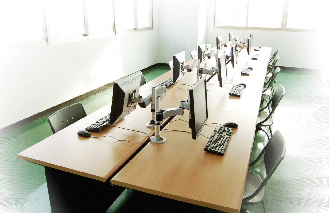Reihe von Computern auf einem Tisch in einem hellen Raum. Alle Bildschirme, Tastaturen und Mäuse sind gleichmäßig angeordnet.
