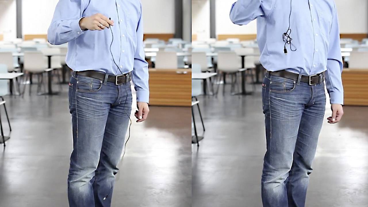 Eine Person in Jeans und blauem Hemd steht in einem leeren Klassenraum. In der Hand hält sie Kopfhörer.