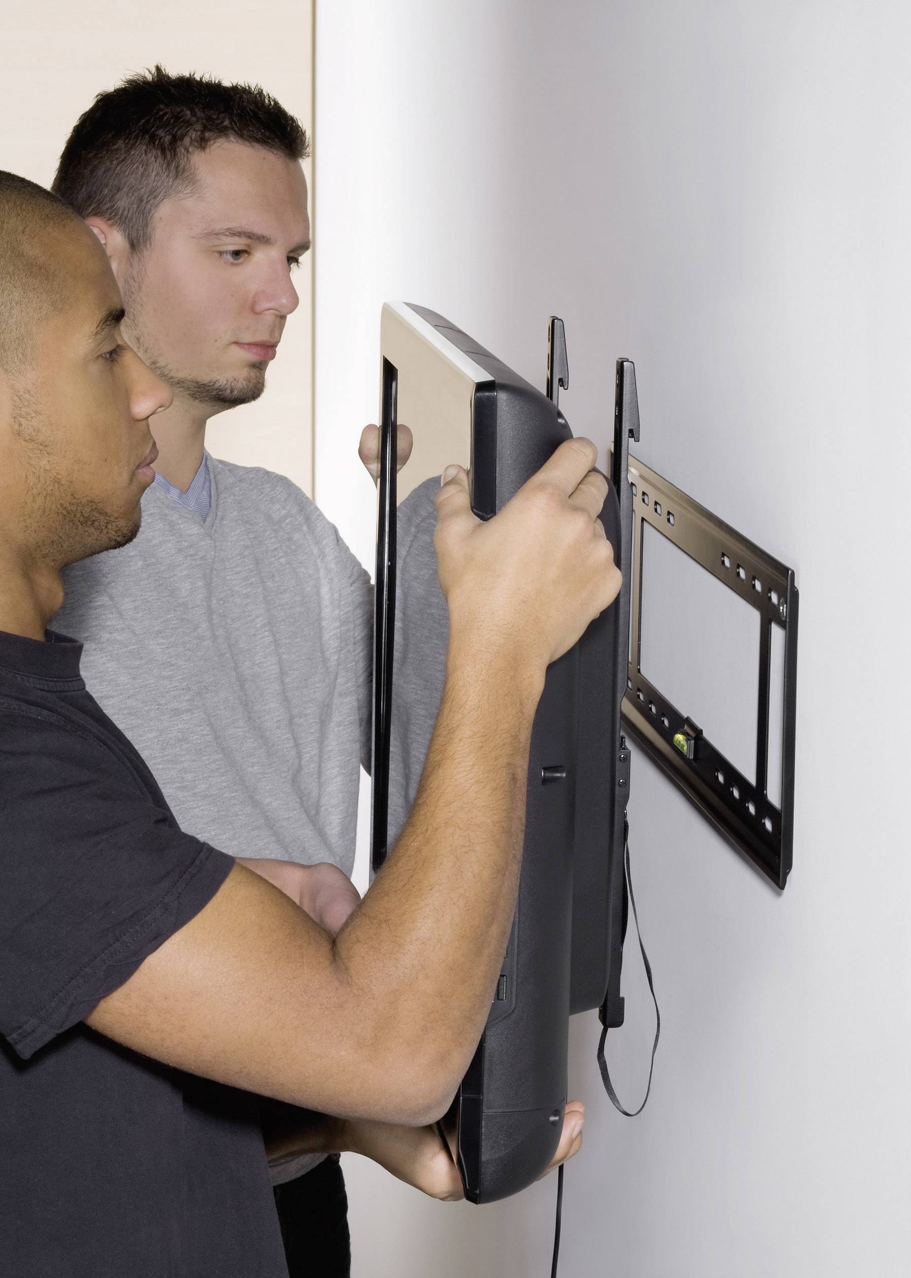 Zwei Männer montieren einen Fernseher an eine Wandhalterung. Der Fernseher wird gerade an der Halterung befestigt.