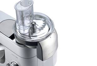 Nahaufnahme eines Edelstahl-Küchenmaschinen- oder Mixers mit durchsichtigem Kunststoffdeckel und zentralem Einfüllschacht.