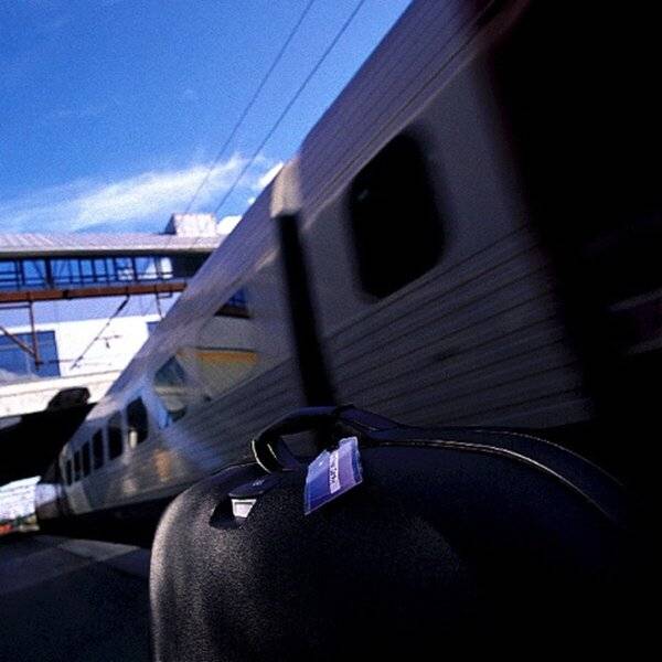 Ein verschwommener Zug, der einen Koffer auf einem Bahnsteig unter blauem Himmel passiert, was auf eilige Reisen oder Abreise hindeutet.