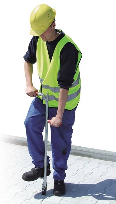 Bauarbeiter mit gelbem Schutzhelm und reflektierender Weste, der ein Handwerkzeug auf dem Gehweg im Freien verwendet.