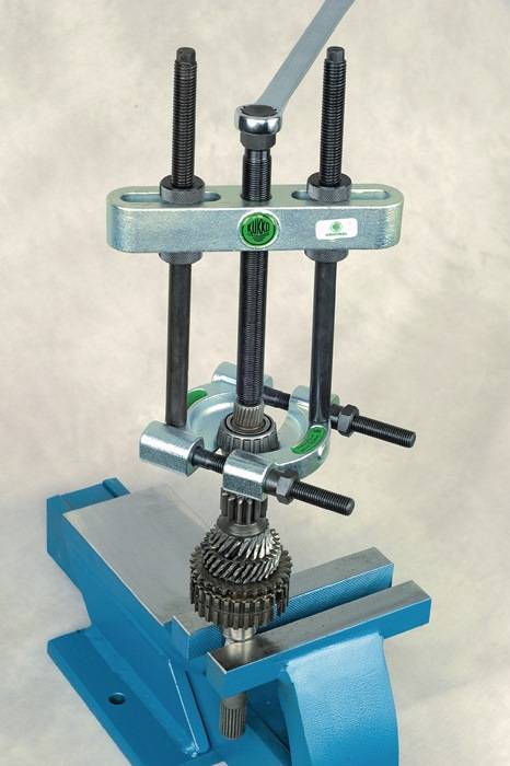 Ein mechanischer Zahnradabzieher ist auf einer Werkbank montiert, umgreift ein Zahnrad und ist bereit, es abzuziehen.