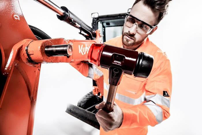 Arbeiter in orangefarbener Schutzausrüstung, der ein hydraulisches Rettungswerkzeug verwendet, um einen beschädigten orangefarbenen Fahrzeugrahmen in einer Werkstatt zu schneiden oder zu spreizen.