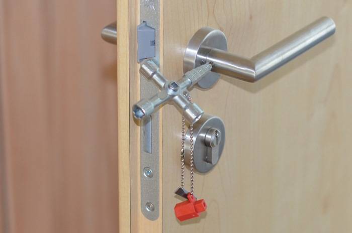 Eine Tür mit einem Griff und einem Verschlussmechanismus, ausgestattet mit einem einzigartigen Vierwege-Schlüssel, der in das Schloss gesteckt ist, mit einem Schlüsselanhänger.