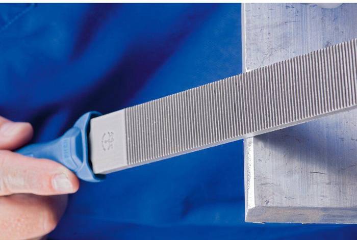 Eine Metallfeile, die zum Glätten der Kante eines Metallblocks verwendet wird, zeigt präzise Feiltechnik.