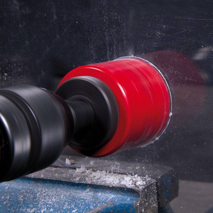 Ein roter Polierradscheibe dreht sich schnell gegen eine Metalloberfläche und erzeugt eine glänzende, glatte Oberfläche. Staub und Partikel verteilen sich dabei.