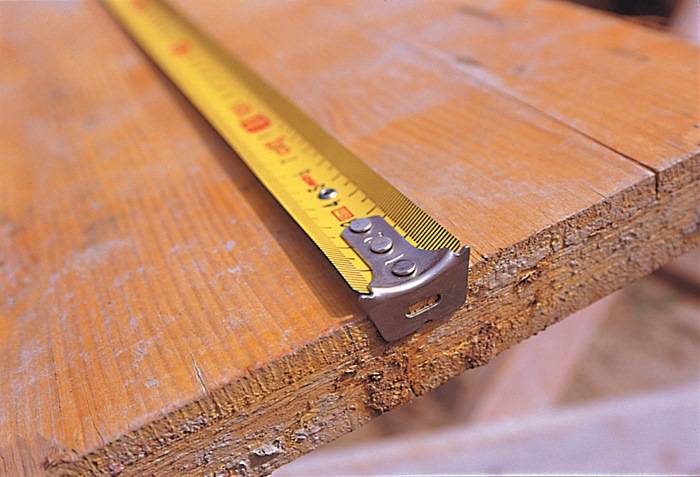 Ein Maßband aus Metall, das über eine Holzoberfläche gewickelt ist und Messmarkierungen zeigt. Das Holz ist grob geschnitten und betont einen DIY-Kontext.