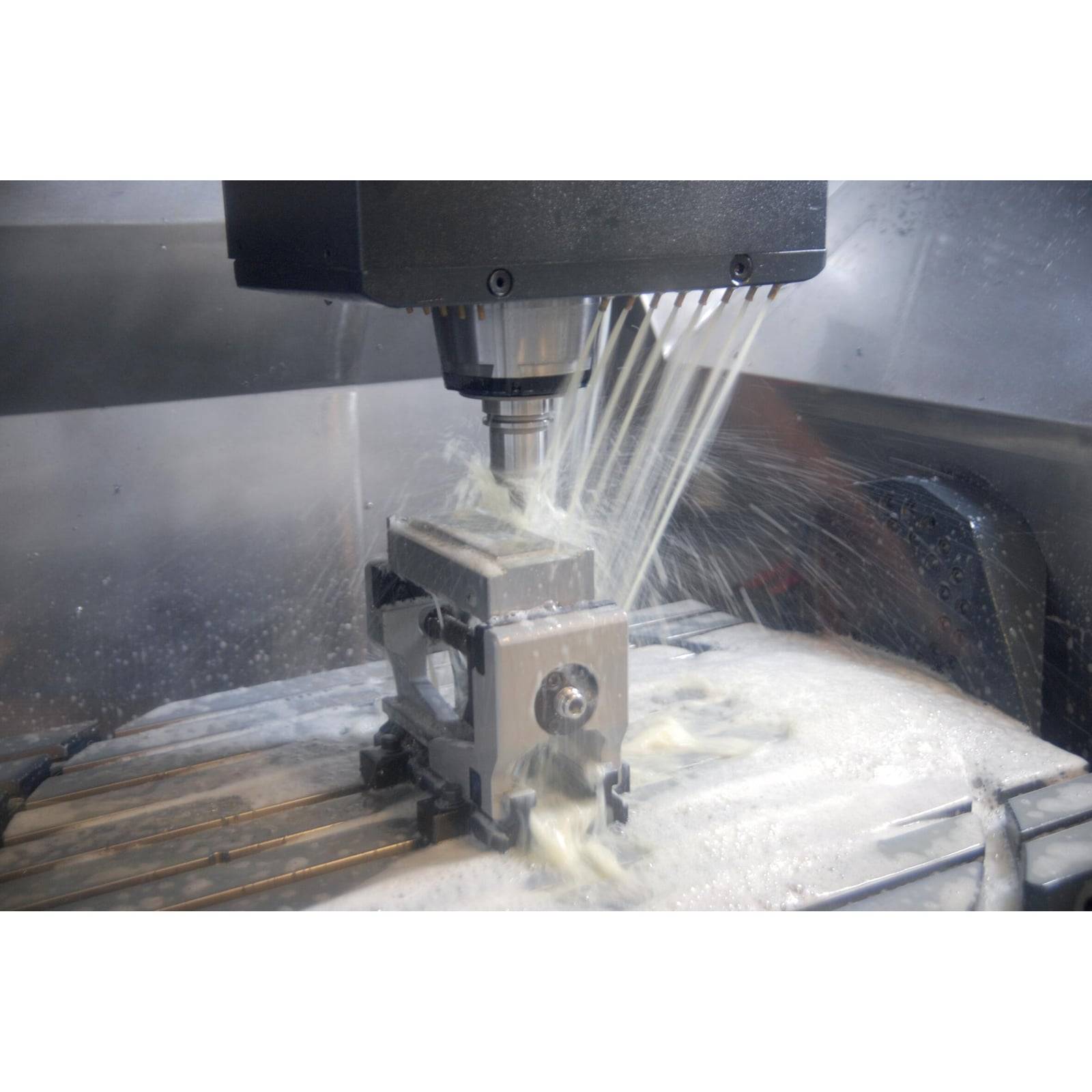 „CNC-Maschine fräst ein Metallteil, Kühlmittel fließt über das Werkstück, in einer Werkstattumgebung. Die Maschine ist in Betrieb.