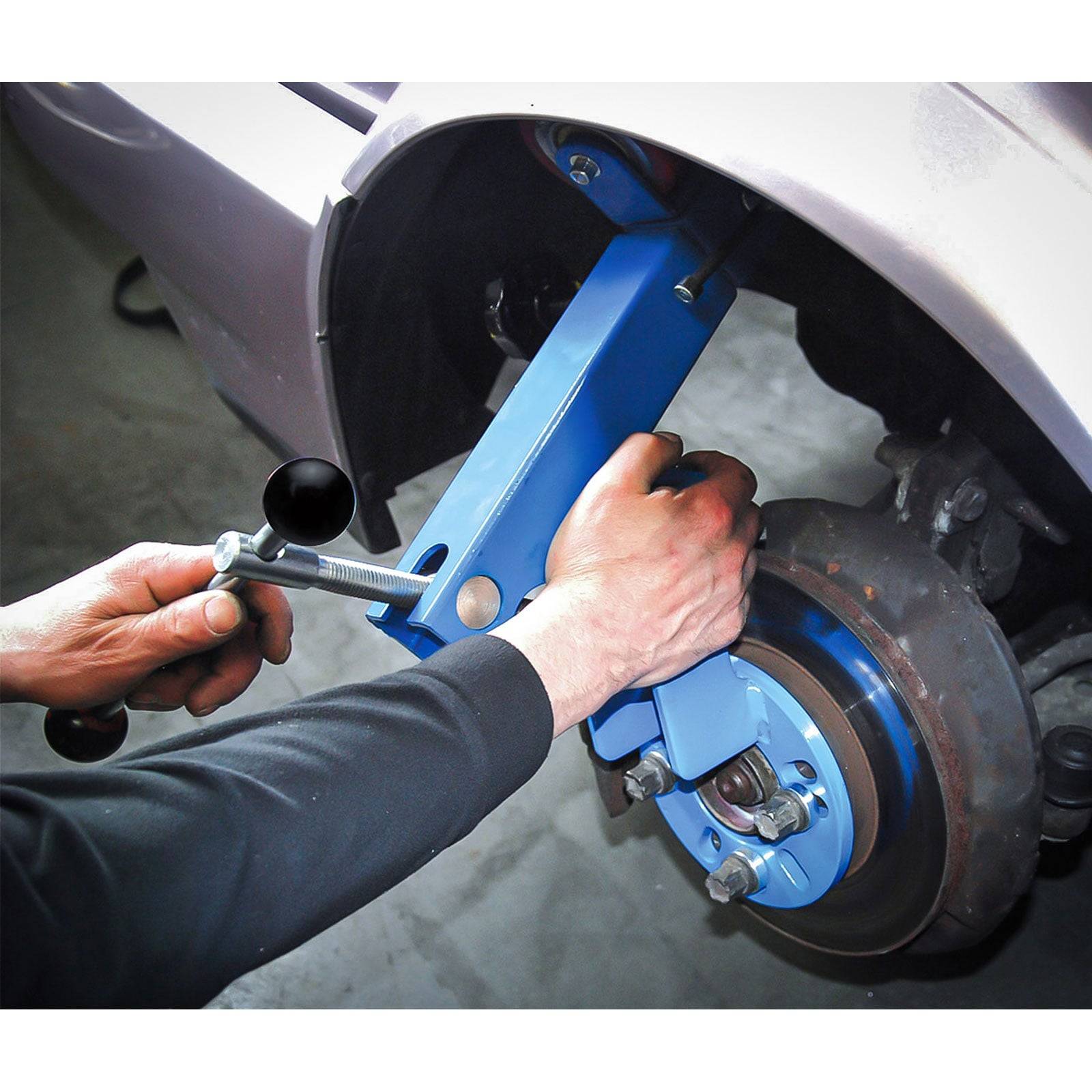 Eine Person verwendet ein blaues Werkzeug, um die Radausrichtung eines Autos einzustellen und demonstriert damit eine Technik zur Fahrzeugwartung.