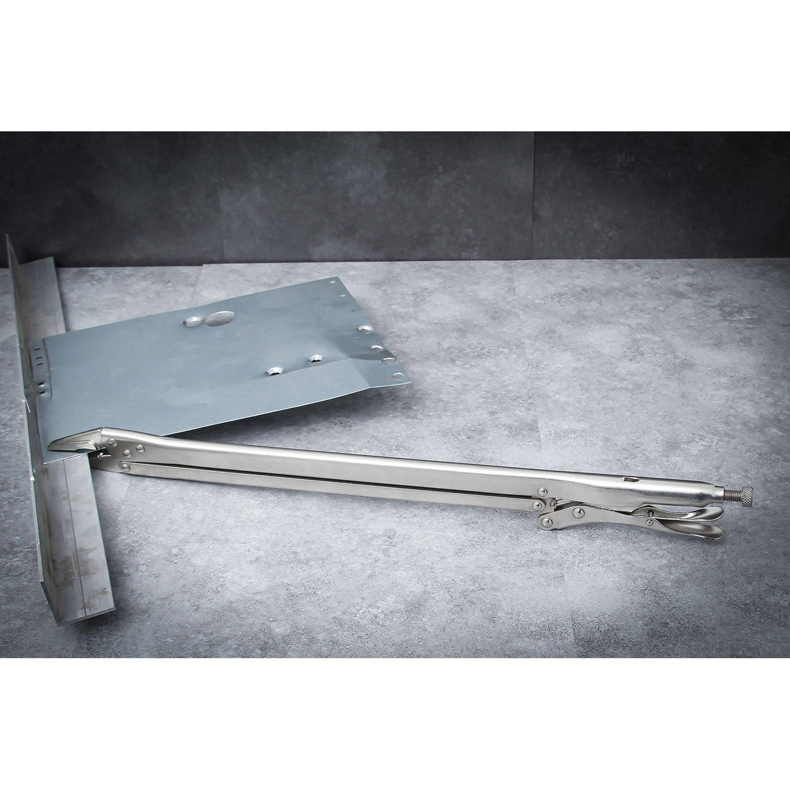 Eine Metallstein-Hebeklemme auf einer grauen Oberfläche, die ihren langen Griff und den Greifmechanismus zum Handhaben großer flacher Objekte zeigt.