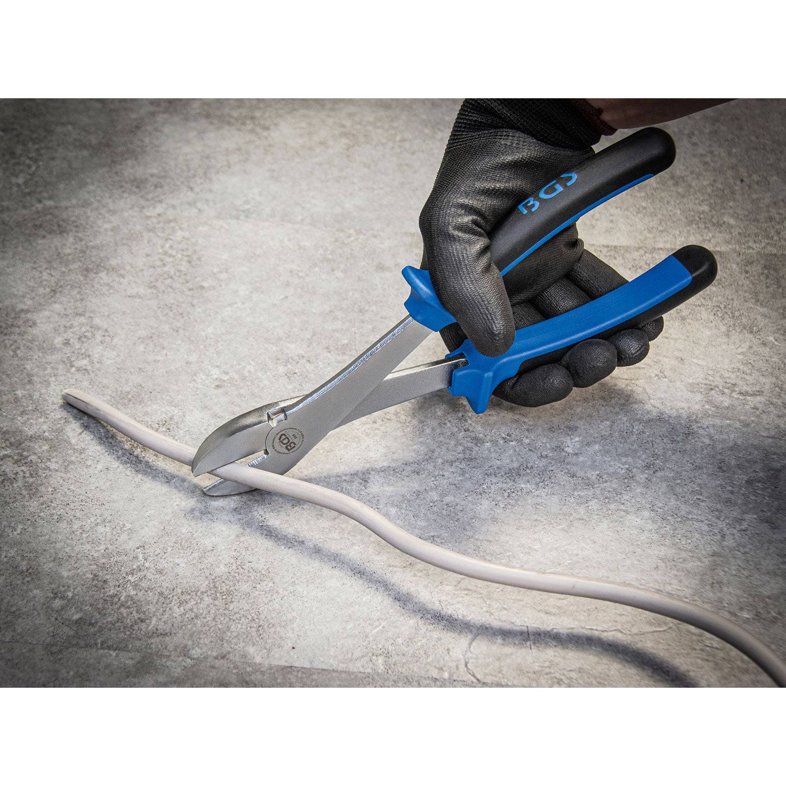 Eine Handschuh tragende Hand verwendet eine Zange mit blauen Griffen, um einen grauen Draht auf einer rauen grauen Oberfläche zu durchtrennen.