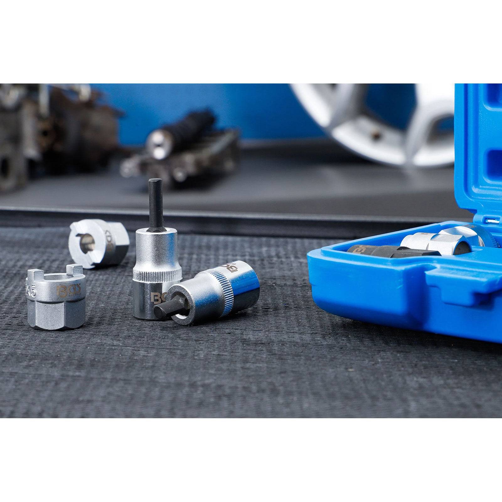 Eine Reihe von Metallsteckschlüssel-Adaptern in einer blauen Tasche auf einer dunklen Oberfläche, unscharfer Hintergrund mit mechanischen Teilen.