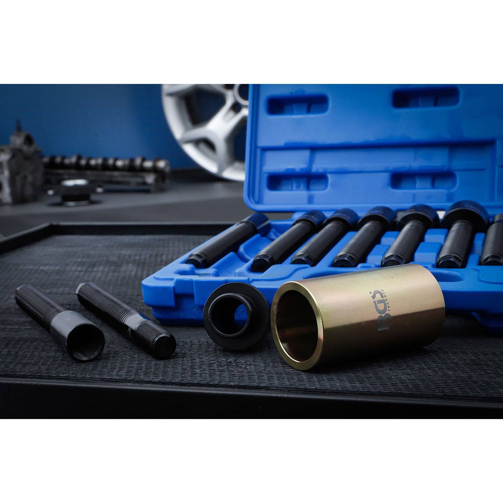 Ein Satz Radschloss-Entfernungswerkzeuge in einem blauen Kunststoffkoffer auf einem Werkstatttisch, mit einem Autoreifen im Hintergrund.