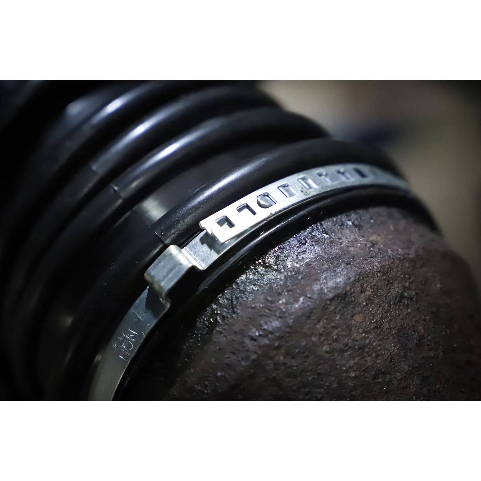 Nahaufnahme einer Metallklemme, die einen flexiblen schwarzen Gummischlauch um eine strukturierte braune Oberfläche befestigt und damit den Einsatz industrieller Ausrüstung veranschaulicht.