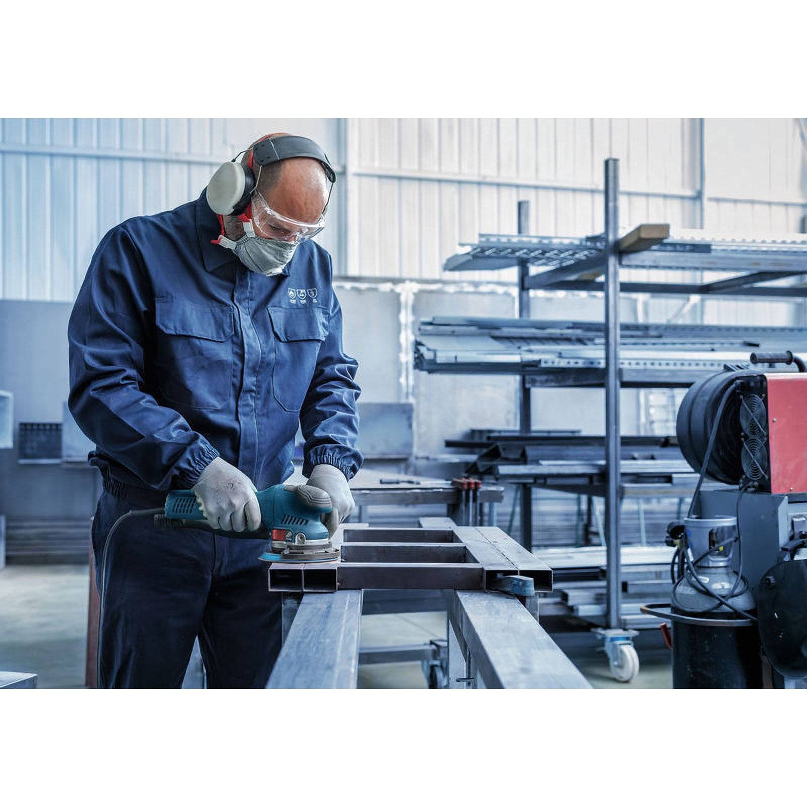 Ein Arbeiter in Schutzausrüstung verwendet ein Elektrowerkzeug, um Metallträger in einer Industriewerkstatt zu schneiden, wobei er sich konzentriert auf die Aufgabe und unter Einhaltung von Sicherheitsmaßnahmen.