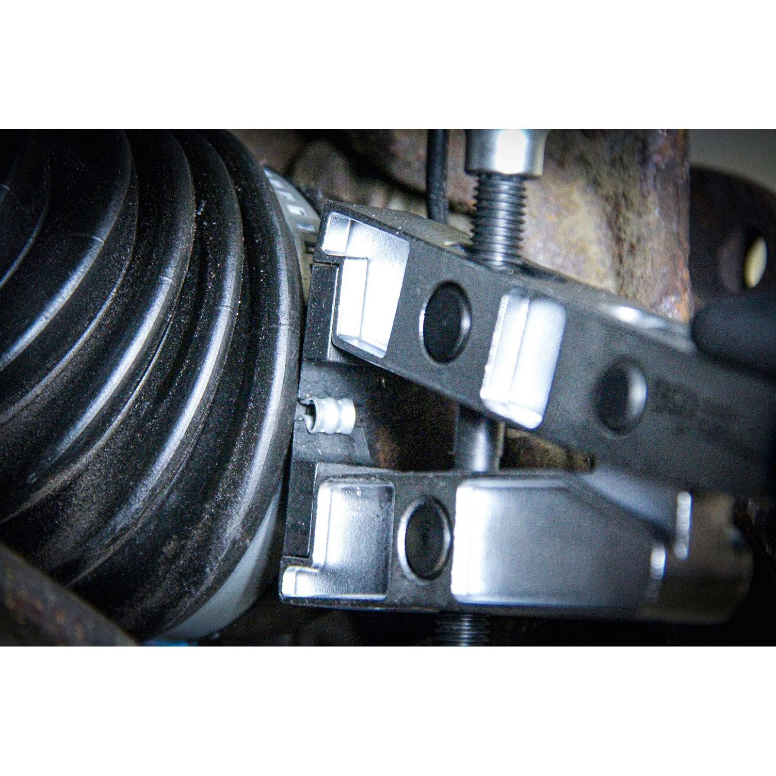 Eine Nahaufnahme einer mechanischen Komponente, die eine Metallklemme zeigt, die einen Gummibalg an einem Autoteil fest fixiert, höchstwahrscheinlich für eine Reparatur oder Wartung.