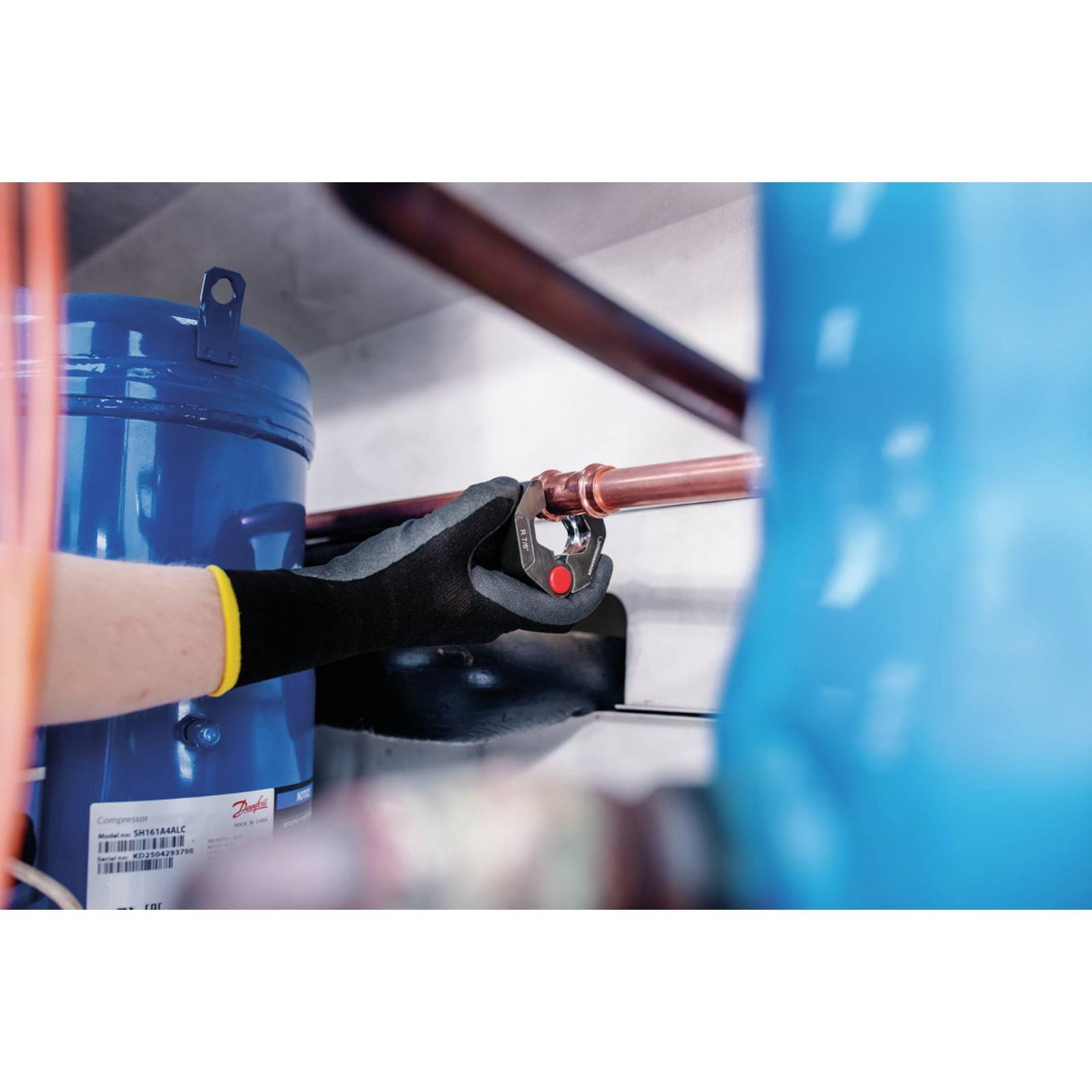Eine Person mit einem schwarzen Handschuh hält ein Werkzeug, um ein Ventil an einer Kupferrohrleitung neben einem blauen industriellen Zylinder und Kabeln einzustellen.