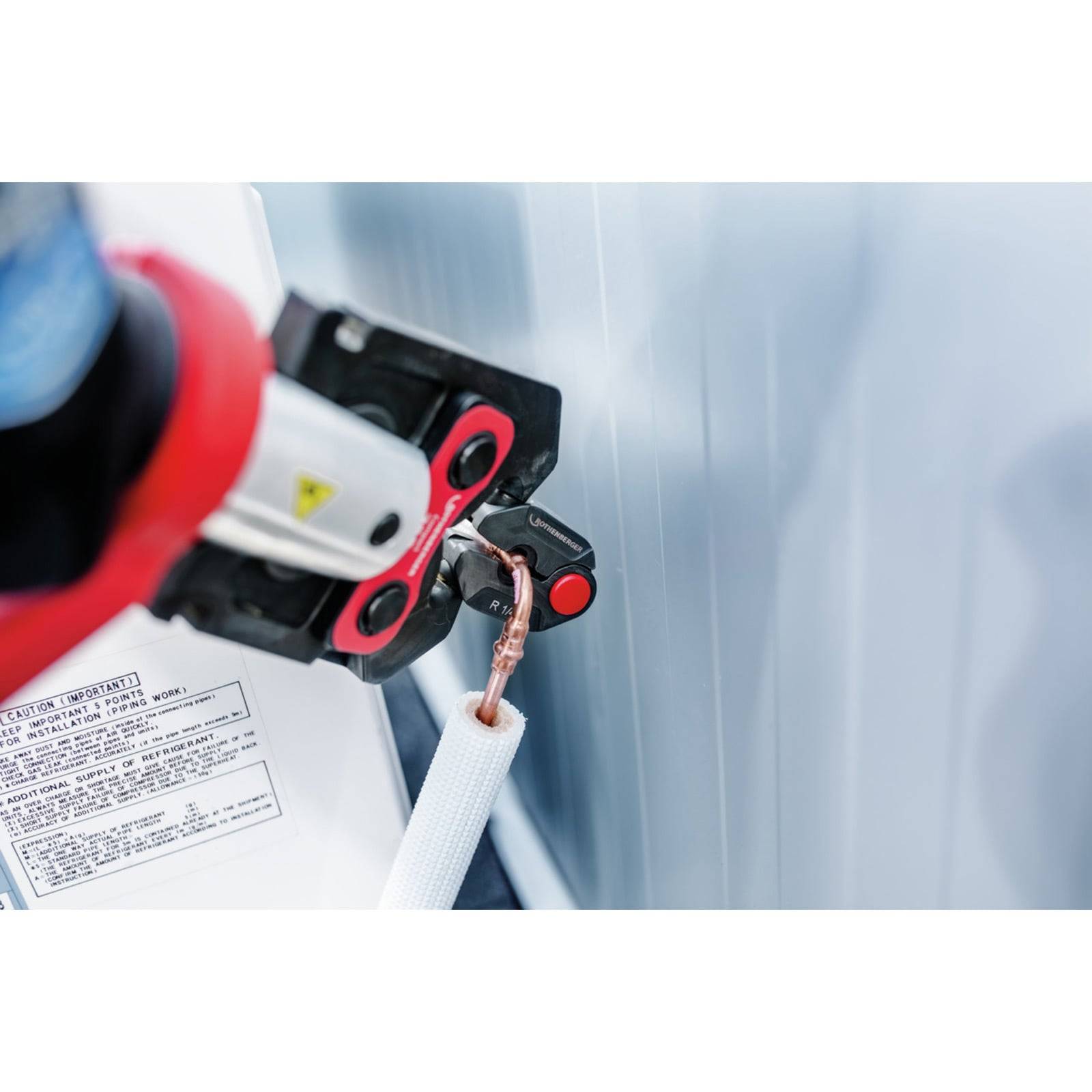 Eine hydraulische Crimpzange komprimiert eine Kupferdrahtschelle und verbindet sie sicher mit einem weißen Kabel über eine Metalloberfläche.