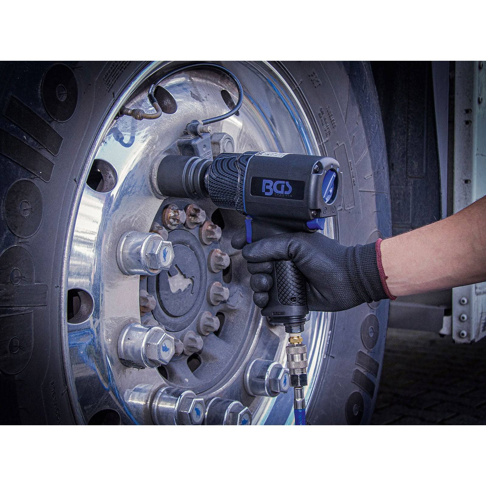 Eine Person in einem Handschuh verwendet ein Elektrowerkzeug, um eine Radmutter an einem großen Lastwagen-Rad zu lockern. Das Werkzeug ist mit einem Luftschlauch verbunden.